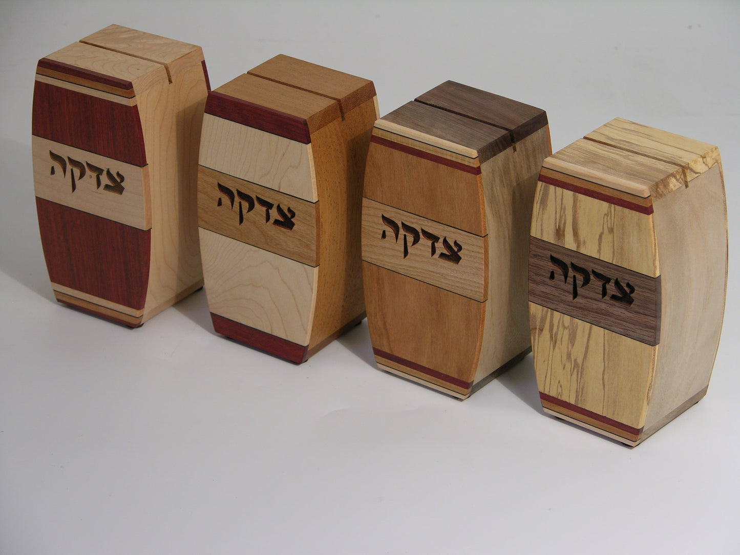 Set of four EC13 tzedakah boxes, left to right: EC13A bloodwood/maple, EC13B maple/cherry, EC13C cherry/cherry, EC13D spalted maple/walnut; arched profile with inlaid hardwood strips.