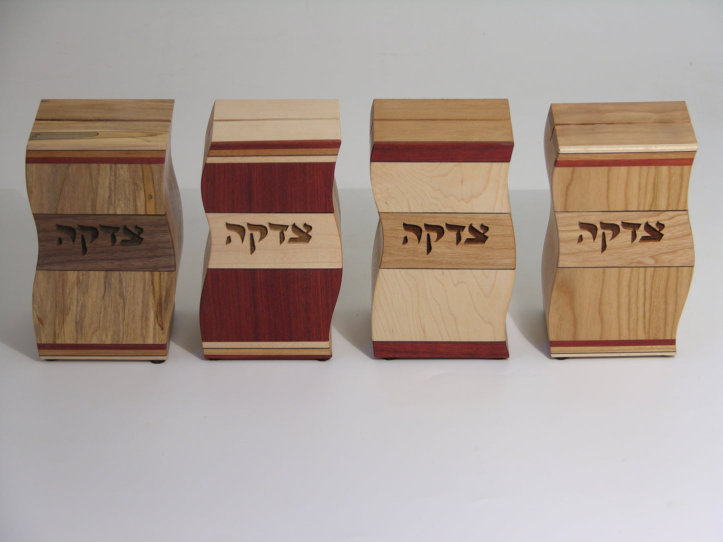 Set of four EC15 tzedakah boxes, left to right: EC15A ambrosia maple/walnut, EC15B bloodwood/maple, EC15C maple/cherry, EC15D cherry; wavy profile with inlaid strips.