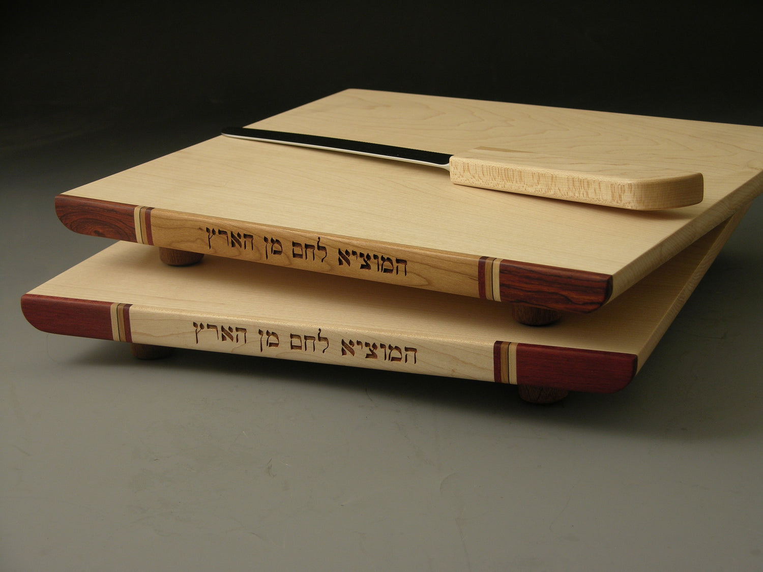 Challah Boards (EC33) featuring maple wood with laser-engraved Hebrew 'emotzi' text, inlaid hardwood accents, and a matching Sheffield knife. Ideal for Shabbat meals.