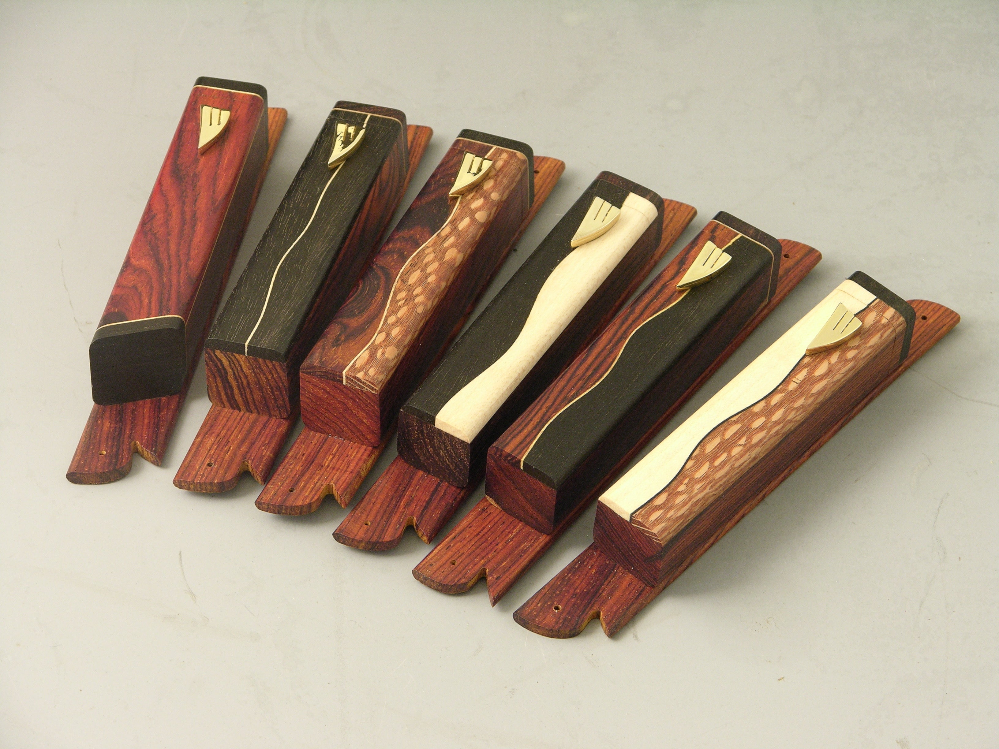 Set of six EC2 mezuzah cases, left to right: EC2A cocobolo, EC2B ebony/ebony, EC2C cocobolo/lacewood, EC2D ebony/maple, EC2E cocobolo/ebony, EC2F maple/lacewood; gold-plated shin.